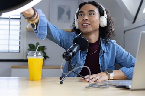 Nonbinary creator adjusting ring light in home podcast studio with headset and microphone