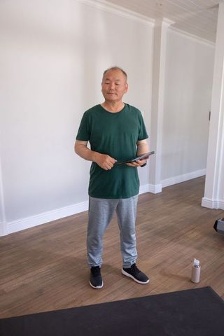 Senior asian man holding tablet preparing for home workout in bright minimalist room