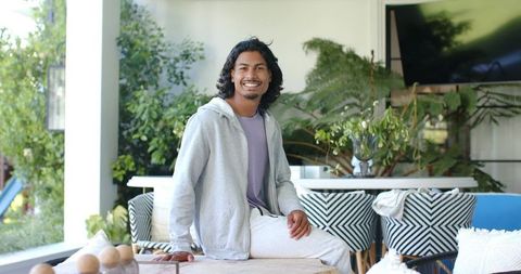 Smiling african american man sitting on low table in sunlit sunroom surrounded by greenery