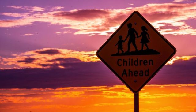 Children ahead sign silhouetting against vibrant sunset sky, backlit roadside warning