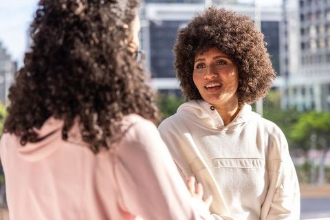 African american women chatting in sunlit urban plaza wearing hoodies casual city conversation