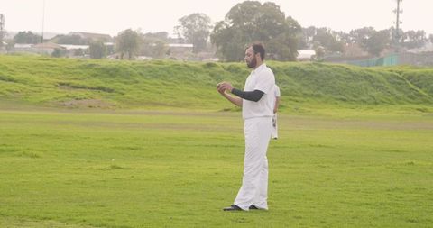 Player Inspecting Cricket Ball on Green Field during Match