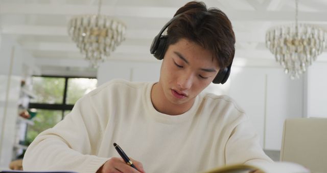 Asian male teenager with headphones learning and sitting in living room. spending time alone at home.