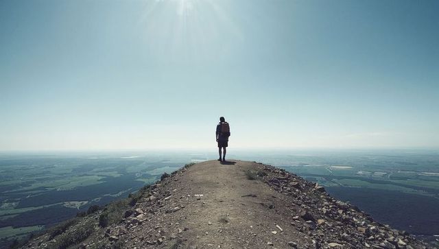 Solo hiker standing on rocky ridge overlooking vast valley and endless horizon