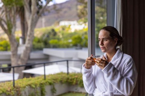 Woman in 30s white bathrobe sipping tea on balcony morning serenity overlooking garden