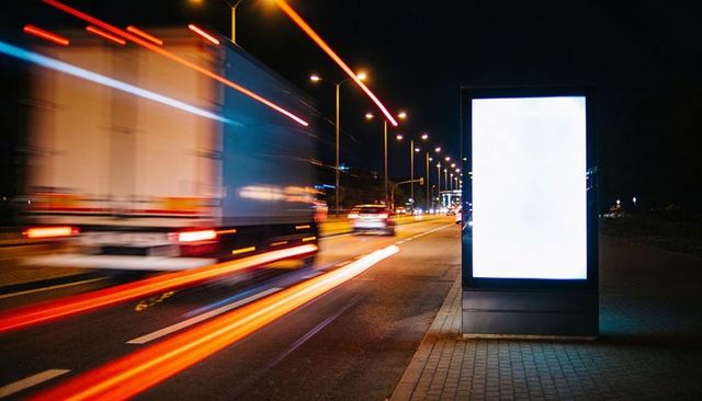Glowing blank digital billboard standing by urban road with motion light trails at night