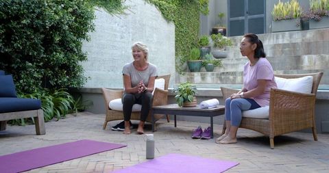 Senior women sitting on wicker chairs in garden courtyard after gentle yoga session
