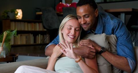 Joyful couple embracing showing engagement ring at home