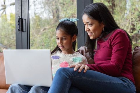 Indian mother teaching daughter on laptop, sharing online learning moment on cozy living room sofa