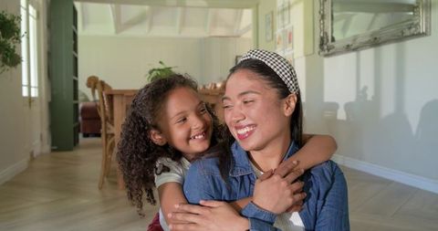 Mother and daughter sharing warm hug and smiling in sunlit cozy home, family embrace