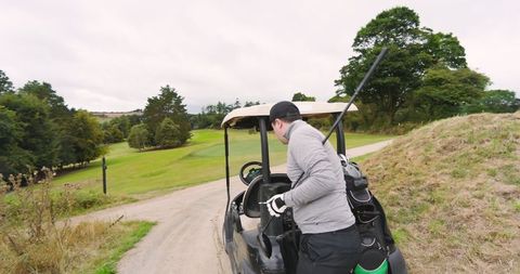 Golfer Arranging Clubs in Cart on Scenic Fairway