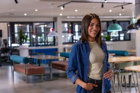 Young woman smiling in modern coworking lounge wearing denim shirt and smartwatch