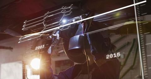 Female welder welding beneath vehicle with augmented reality overlays in industrial workshop