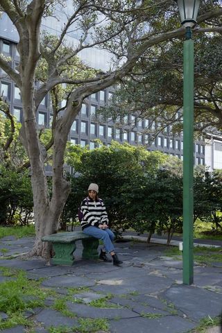 Asian woman sitting on green bench in urban plaza near office building, contemplative lifestyle
