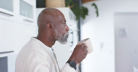 Mature african american man sipping coffee in modern minimalist kitchen, quiet morning moment