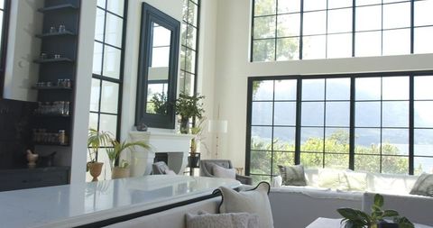 Showcasing sunlit open living space with white marble island and black-framed industrial windows