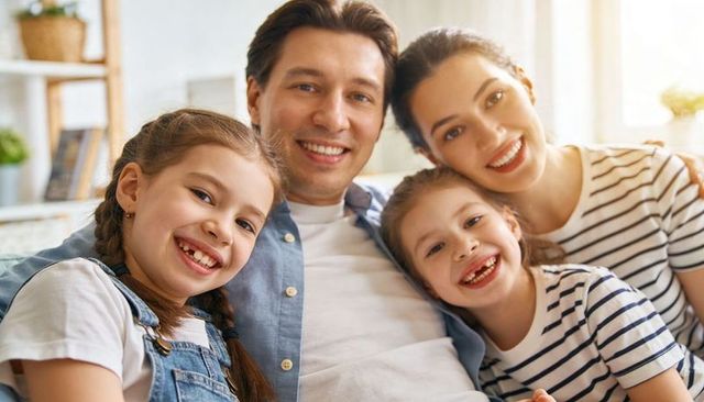Smiling family cuddling on sunlit sofa parents with two daughters sharing warm moment