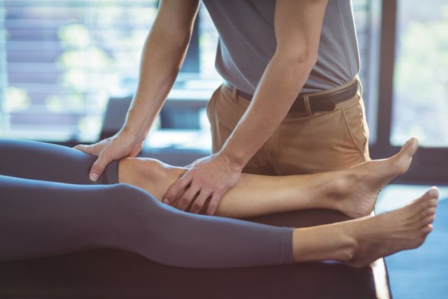 Physiotherapist performing knee therapy on a female patient in a clinic. Useful for illustrating medical treatments, physical therapy sessions, rehabilitation processes, and healthcare services. Ideal for use in healthcare websites, medical brochures, and wellness blogs.