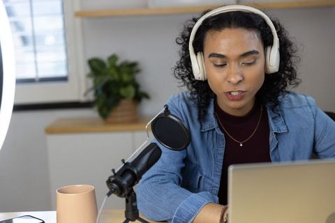 Non-binary creator recording podcast in home studio with headphones and microphone