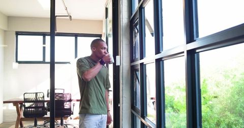 African man sipping coffee by glass window in contemporary coworkorking office checking watch
