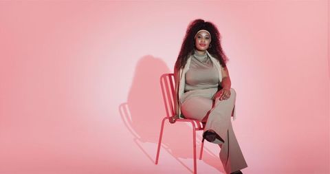 Confident Woman in Beige Suit Sitting on Chair With Pink Background
