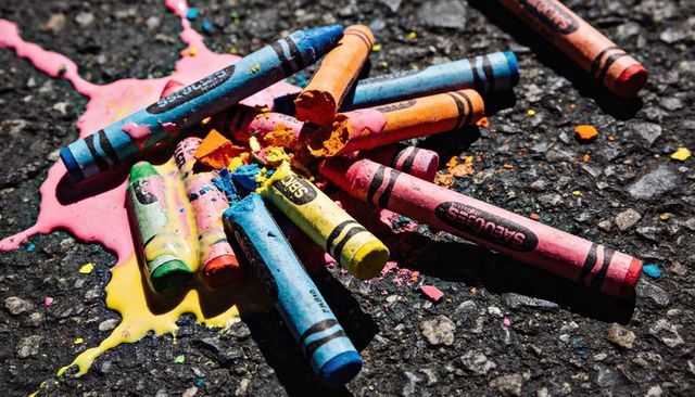Melting crayons on asphalt with bright color splashes and broken wax fragments