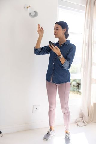 Asian woman checking smartphone by window in minimalist bright home interior wellness
