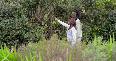 African American man and Indian woman walking nature trail pointing toward green foliage