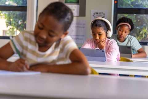 Multicultural girls learning with tablets in classroom wearing headphones, focusing