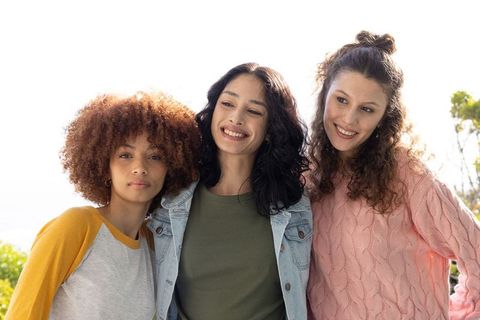 Sunlit diverse women smiling together outdoors in casual clothes celebrating friendship