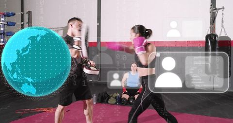 Female boxer training with coach hitting focus mitts in boxing gym with digital globe and ui overlay