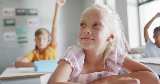 Image of happy caucasian girl raising hand during lesson in classsroom. primary school education and learning concept.