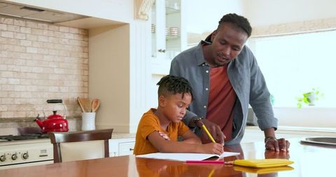 Father helping son with homework in bright kitchen setting
