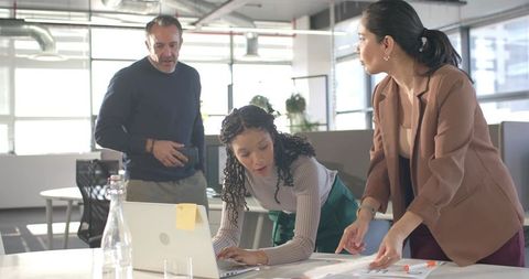 Diverse team collaborating over laptop and documents in modern open-plan office