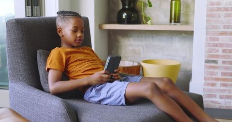 Young boy relaxing on armchair using smartphone in modern living room