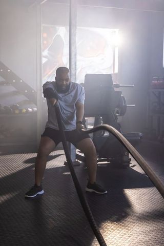 African american man performing intense battle-ropes workout in backlit gym for strength