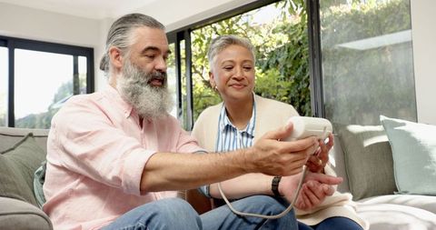 Senior couple using digital blood pressure monitor in living room