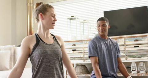 Diverse friends stretching together in sunlit living room wearing casual sportswear for yoga