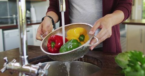 Pregnant woman washing bell peppers in modern kitchen