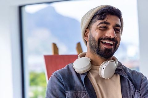 Creative young bearded man wearing beanie and headphones smiling in bright art studio