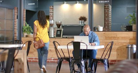 Male entrepreneur working on laptop in industrial coffee shop with wooden counter