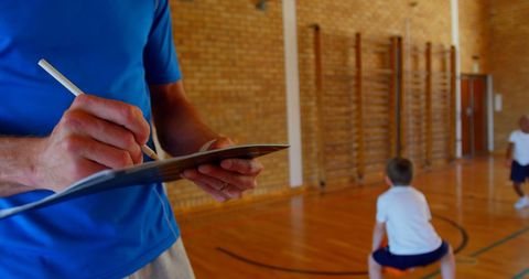 Coach Taking Notes in School Gym During Basketball Practice