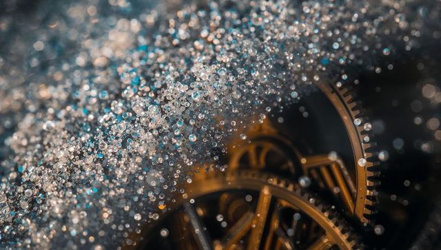Macro brass clockwork gears reflecting warm studio light with sparkling droplet bokeh