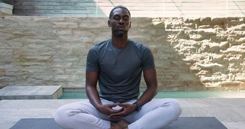 Man meditating outdoors on stone patio by pool's edge