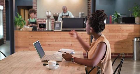African american woman working on laptop and talking to barista in cozy brick coffeehouse