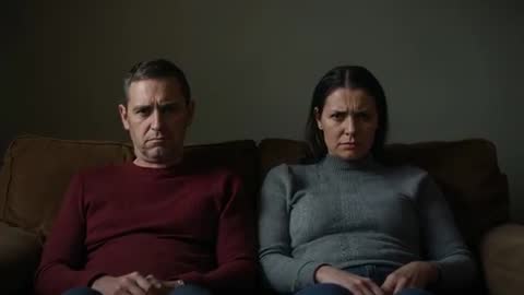 Mature couple sitting tense on couch facing forward expressing relationship conflict