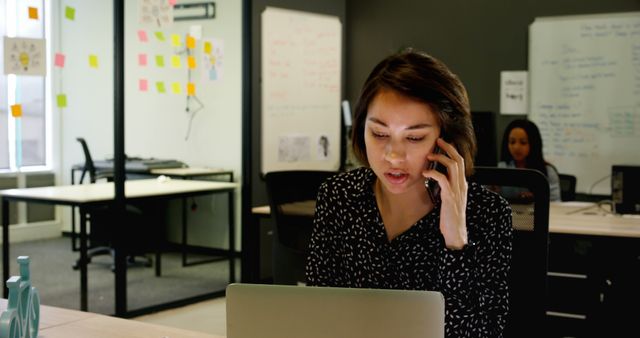 Focused Woman in Office Talking on Phone and Using Laptop - Download Free Stock Images Pikwizard.com