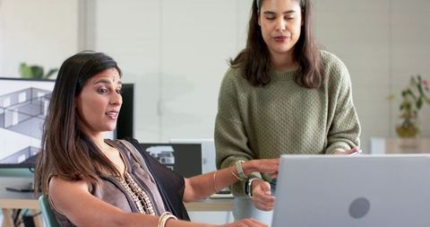 Diverse female coworkers collaborating on architectural plan using laptop and monitor