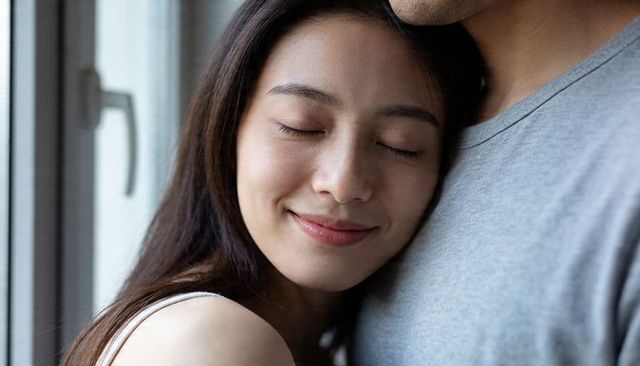 Young woman resting on partner's chest by window, tender intimate moment in sunlight
