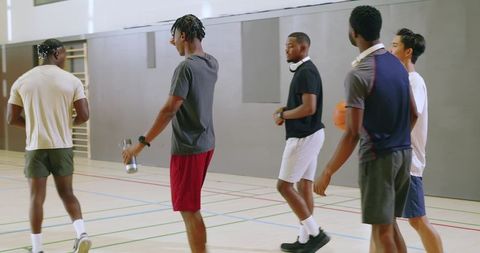Group of young men walking across indoor basketball court carrying ball and water bottle